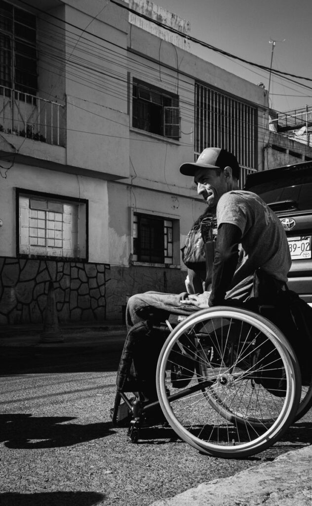 A candid black and white photo of a man in a wheelchair on a city street, capturing urban resilience and independence.