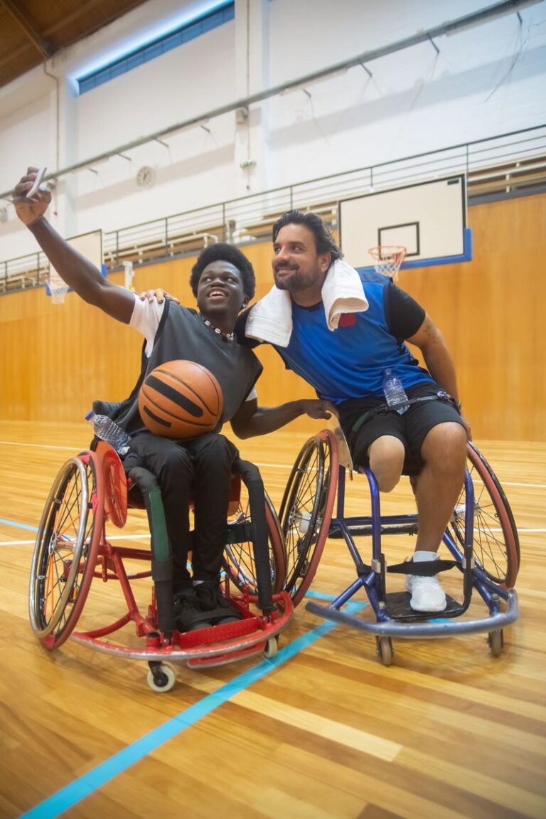 Two wheelchair basketball players smiling and taking a selfie on the court.