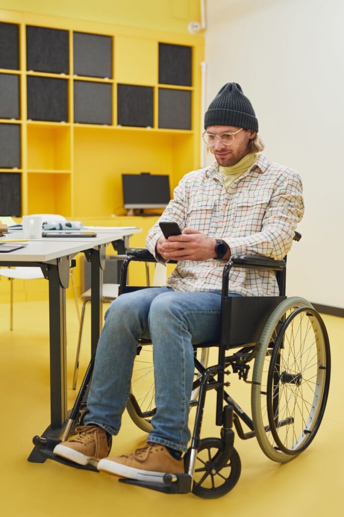 Man in a wheelchair using phone in a modern office, wearing casual attire.